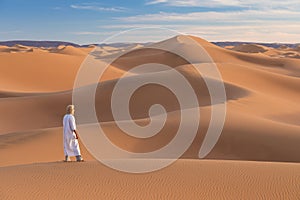 Bedouin on way through sandy desert. Beautiful sunset with big dunes on Sahara, Morocco. Silhouette nomad man.
