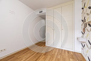 Bedroom with a built-in wardrobe with three white wooden doors, papered walls and French oak flooring