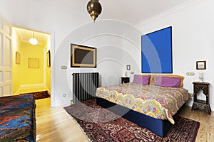 Bedroom with double bed decorated with colorful quilts and rug on pine wood flooring