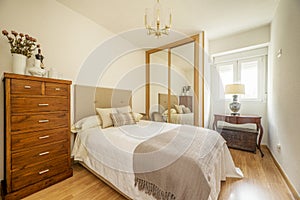 Bedroom with a double bed with a headboard upholstered in beige fabric, a large wooden chest of drawers and a built-in wardrobe on