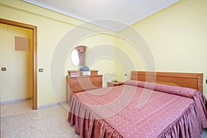 Bedroom with double bed with wooden headboard and hideous pink bedspread