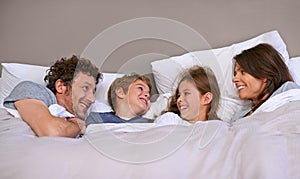 Bedroom, family and parents with children, relax and morning with smile, funny and peaceful. Mother, father and bed with
