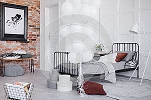 Bedroom interior with grey bedding, bunch of white balloons and black frame on the brick wall, real photo