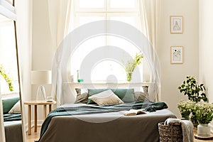 Bedroom interior in nature colors with big bed, gray and green linen and pillows, fresh meadow flowers and a sunny window in the b