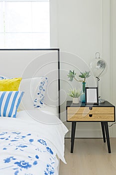 Bedroom interior with striped pillow on bed and bedside table lamp with picture frame on it.