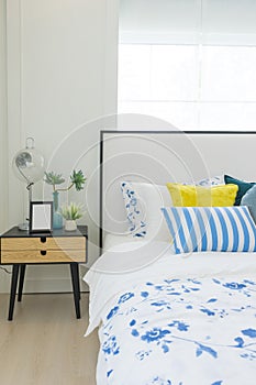 Bedroom interior with striped pillow on bed and bedside table lamp with picture frame on it.