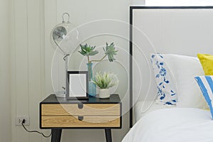 Bedroom interior with striped pillow on bed and bedside table lamp with picture frame on it.