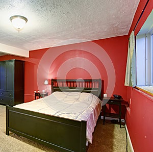 Bedroom with red walls. Black color furniture and beige blanket.