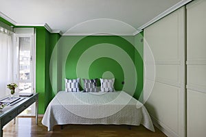 Bedroom in a room with a double bed with cushions, a green wall, a built-in wardrobe with sliding doors and a table with vintage