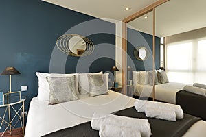 Bedroom with silver cushions, blue colored wall, fitted wardrobe with mirrored sliding doors and matching gold bedside tables with