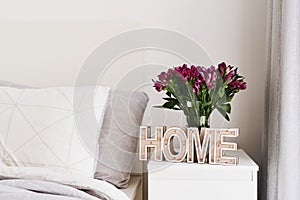 Bedroom simple and cozy decor: wooden `home` sign and fresh flowers in a vase on a bedside table