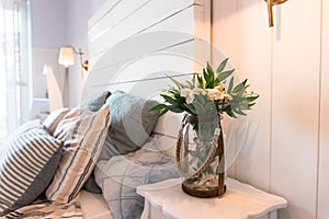 Bedroom in soft light colors. big comfortable double bed in elegant classic bedroom.White flowers in glass vase on a