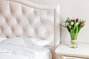 Bedroom in soft light colors. Vase of colorful tulips in light cozy bedroom interior