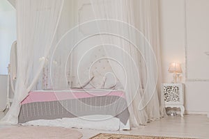 Bedroom in soft light colors with a wooden floor. Big comfortable four poster double bed in elegant classic bedroom