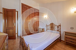 Bedroom with a three-section built-in wardrobe with sapelly wood doors, vintage wooden furniture and a matching wooden access door