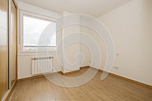 bedroom with a two-section built-in wardrobe with large oak sliding doors and wooden floors, a single-pane aluminum window with