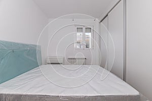 Bedroom with uninstalled bed with protective plastics on, built-in wardrobe and aluminum window in the background photo