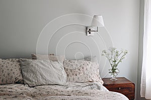 Bedroom view. Striped and floral linen pillows, blanket. Wooden night stand, bedside table Blooming bishops goutweed