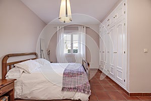 A bedroom with a white duvet with cushions on a wooden double bed next to the window