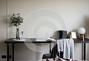 Bedroom working corner decorated with laptop, white candles and artificial plant in glass vase on black wood  working table with
