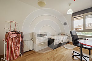 Bedroom with a youthful bed, a study table with a chair on wheels, a white chest