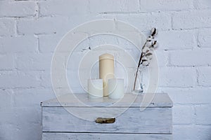 A bedside table with candles and vase with a branch of cotton. Minimalist bedroom interior. Scandinavian style