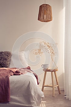 Bedside table with mug and flower next to bed