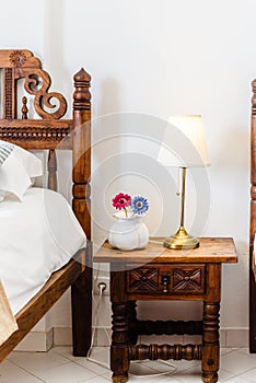 Bedside table with white lamp in the bedroom with vintage wooden bed