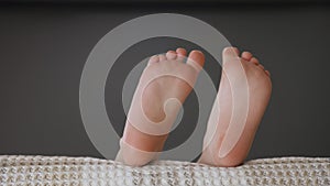 Bedtime child lying in sofa and move of music bare feet close up. Child legs waving in bed having fun barefoot kid