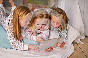 Bedtime just got a whole lot more interactive. three little sisters using a digital tablet before bedtime.