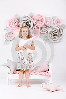 Bedtime. Little girl near bed with pink linen with pillow in the form of a star in her hands in white bedroom with handmade