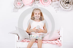 Bedtime. Little girl is sitting on bed with pink linen with pillow in the form of a star in her hands in white bedroom with