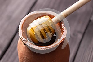 Bee honey in a clay pot on a wooden table. Wooden spatula for honey. Side view, close up. Healthy food. Farm, apiary