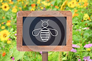 Bee icon on a wooden sign, wild flowers background. Bee conservation zone concept