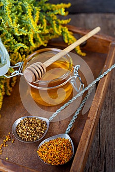 Bee pollen granules. Fresh oney on wooden table. Still life bee product background. Wooden spoon with small glass jar closeup. Eco