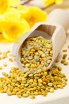 Bee pollen in wooden scoop, yellow flowers