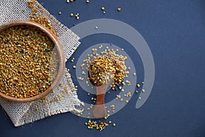 Bee pollen in a wooden spoon healthy food supplements. Close up on a black background. Top view, flat lay. copy space