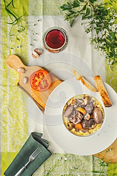 Beef bourguignon in a ceramic plate, tablecloth, fork, flowers