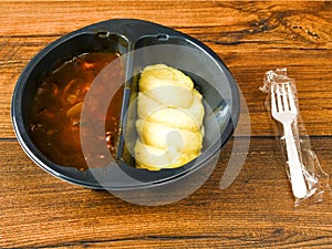 Beef Bourguignon and mash potatoes in a black plastic tray on wooden table and plastic fork. High quality ready meal with premium photo