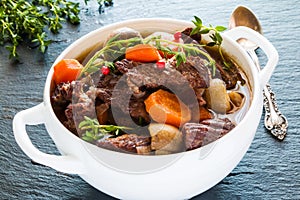 Beef Bourguignon in a white soup bowl on black stone background. Stew with carrots, onions, mushrooms, bacon, garlic and bouquet