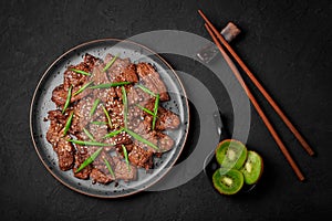 Beef Bulgogi on black plate on dark slate table top. Korean cuisine meat dish with sauce and kiwi. Asian food