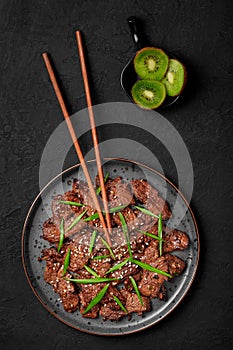 Beef Bulgogi on black plate on dark slate table top. Korean cuisine meat dish with sauce and kiwi. Asian food
