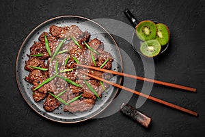 Beef Bulgogi on black plate on dark slate table top. Korean cuisine meat dish with sauce and kiwi. Asian food