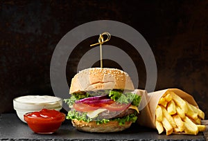 Beef burger, french fries, sauce on a black slate plate on a dark background, fast food, homemade hamburger