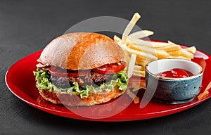 Beef burger and french fries with tomato sauce on red plate over dark background. Unhealthy food