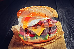 Beef burger with melted cheese and bacon and egg on wooden background