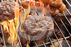 Beef burger and sausages cooking over flames on grill