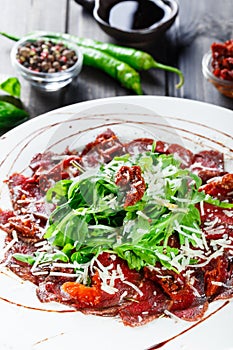 Beef carpaccio with arugula, sun-dried tomatoes, and cheese parmesan on dark wooden background. Delicious appetizers.