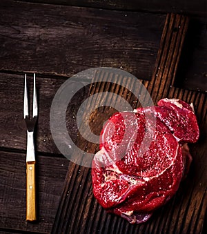 Beef on a chopping board and fork on dark wooden table. Style rustic.