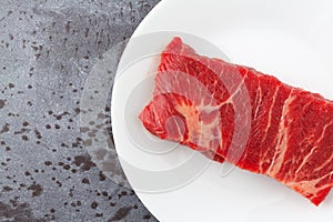 Beef chuck boneless short rib steak on a white plate on a gray counter top